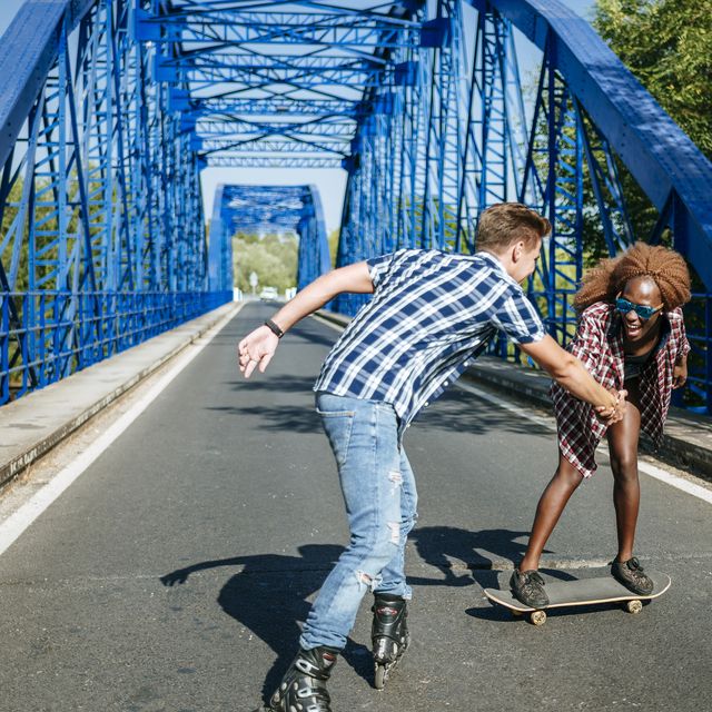 Happy young couple with inline skates and skateboard on a bridge