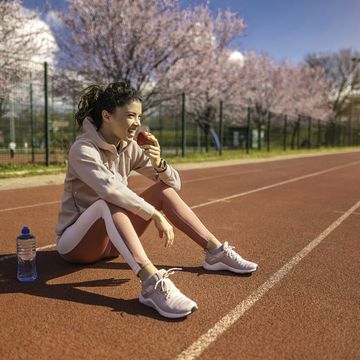happy young female athlete eating an apple on sports track.