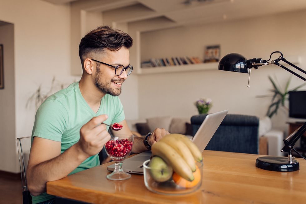 happy young man eating fruits and working at home