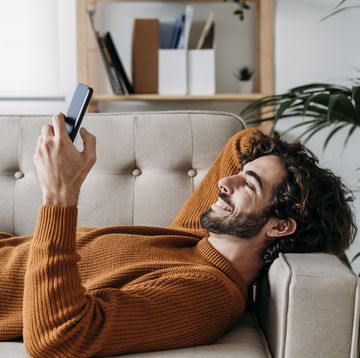happy young man using smart phone relaxing on sofa at home