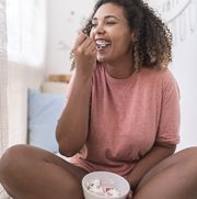 happy young woman eating strawberries with cream while sitting at home
