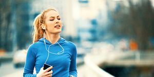 Happy Young Woman Listening Music While Jogging On Bridge