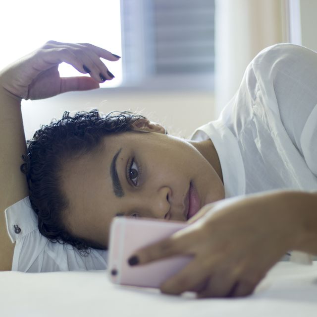 Happy young woman looking at mobile phone in bed