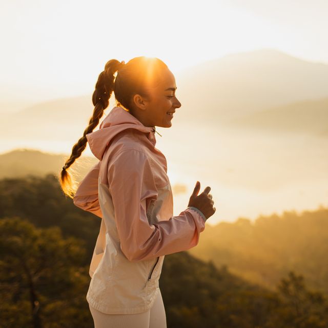 happy young woman running outdoors with mountain view at sunset