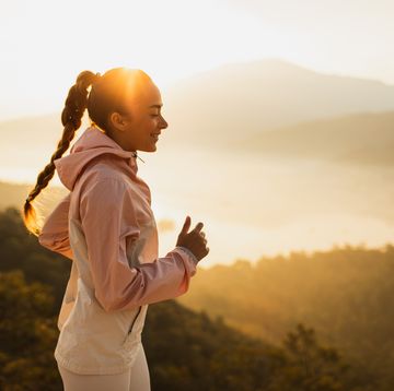 happy young woman running pronadores outdoors with mountain view at sunset