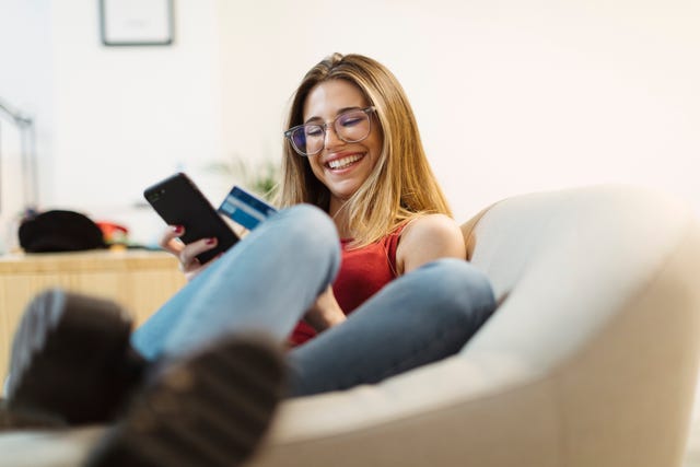 Happy young woman using smartphone and credit card in the office