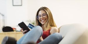 Happy young woman using smartphone and credit card in the office
