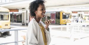 Happy young woman with earphones using smartphone at station platform