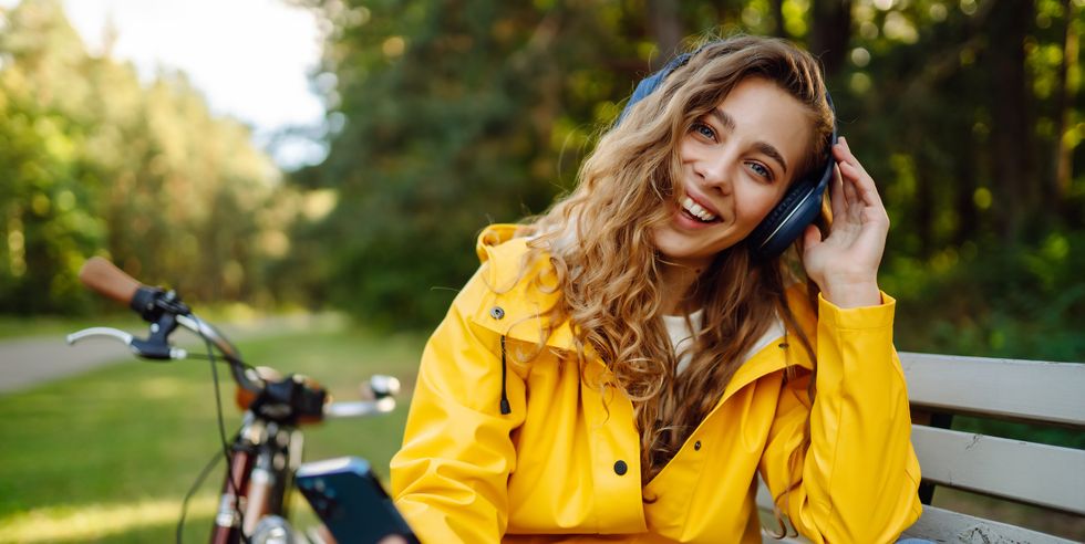 happy young woman with headphones and smartphone rides a bicycle in a sunny park listening to music
