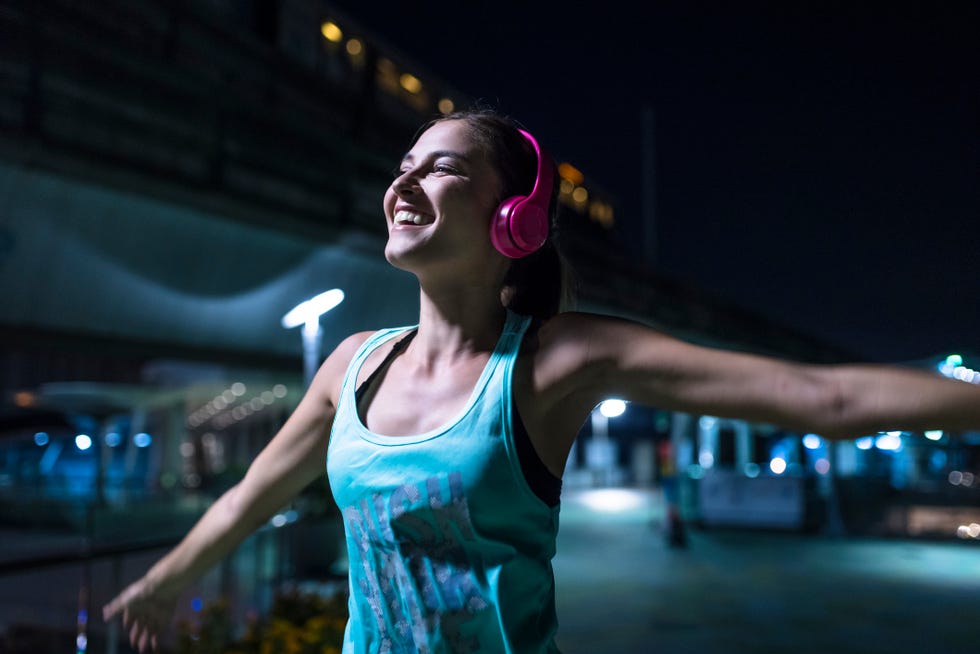 Happy young woman with pink headphones listening to music in modern urban setting at night