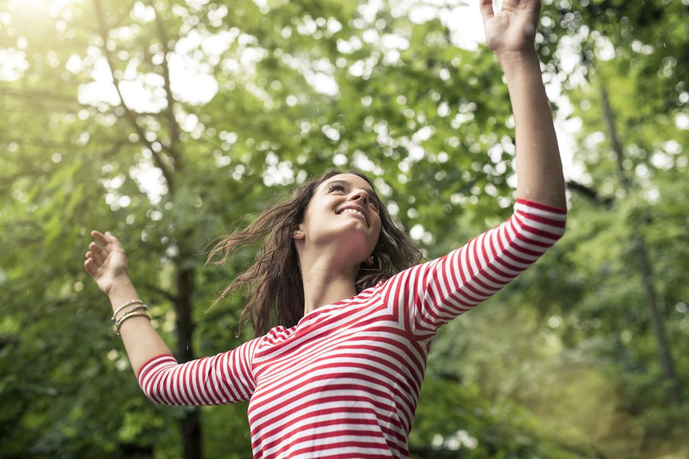 happy young woman with raised arms dancing in nature