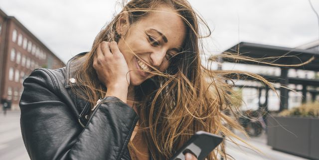Happy young woman with windswept hair using cell phone in the city