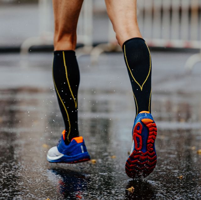 feet male runner in compression socks running on wet asphalt
