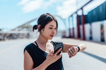 een vrouw kijkt op haar sporthorloge en telefoon tijdens het hardlopen