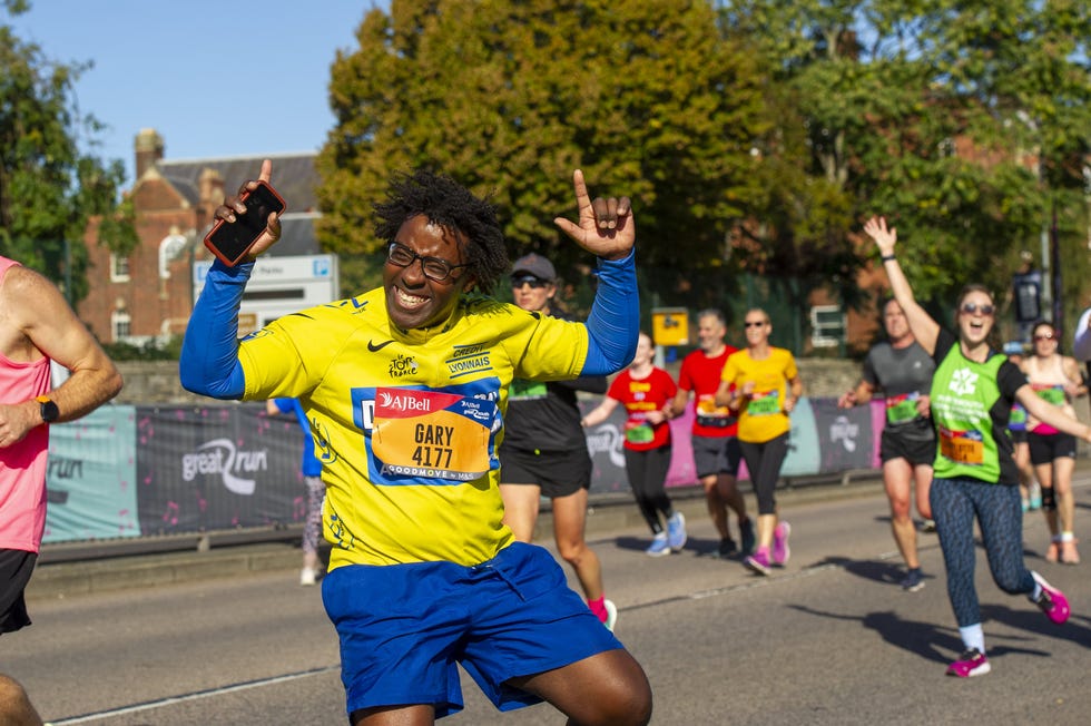 a group of marathon runners is seen on a lively city street, with one individual in a bright yellow shirt striking a celebratory pose