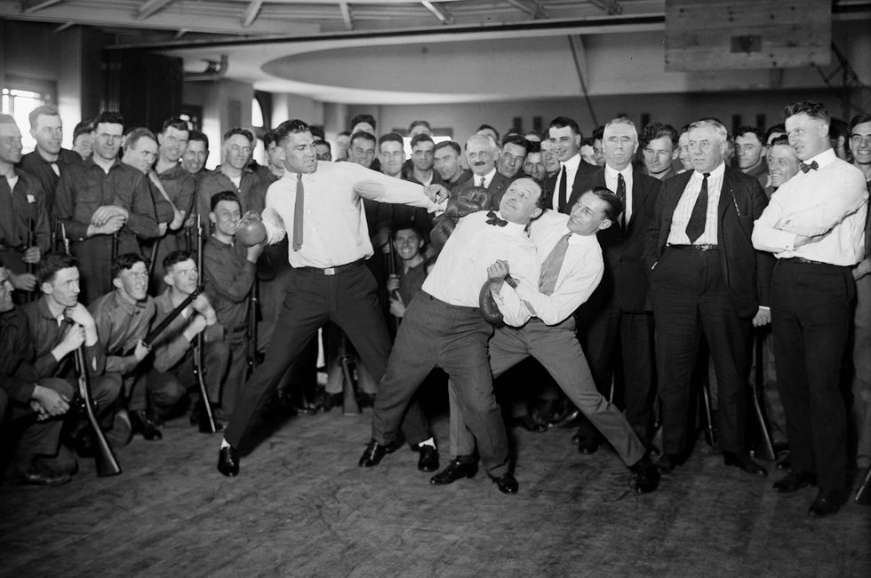 harry houdini cannot escape the hold of boxer benny leonard and jack dempsey prepare to swing