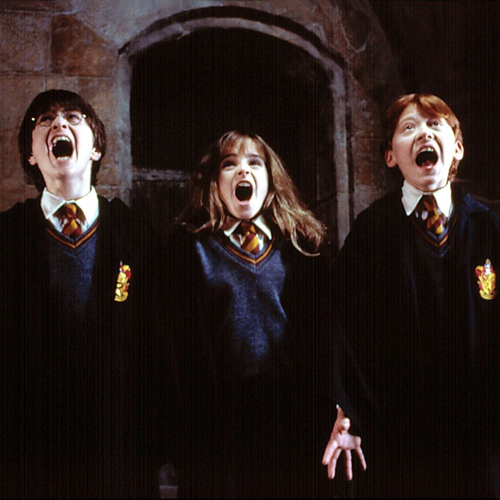 three students in hogwarts uniforms standing together in a dimly lit setting