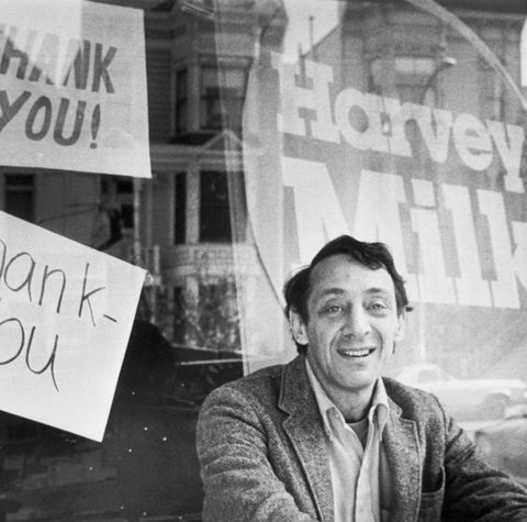 a man in a suit jacket and collared shirt sits down with hands on knees and smiles at the camera