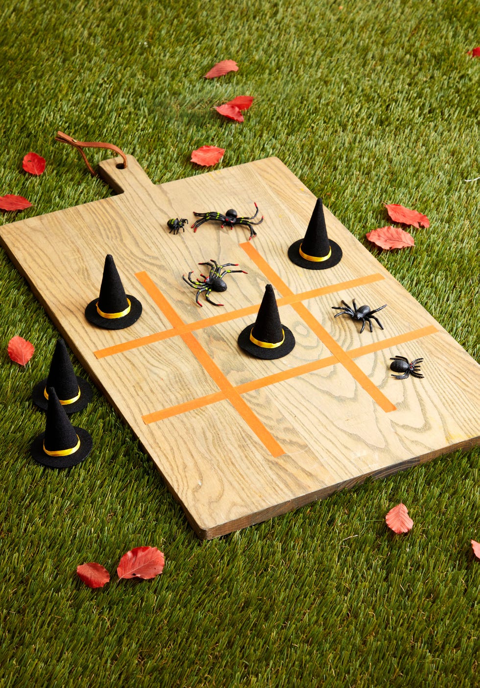 a tic tac toe game made on a wooden cutting board with tape and mini witches hats and plastic spider as the game pieces