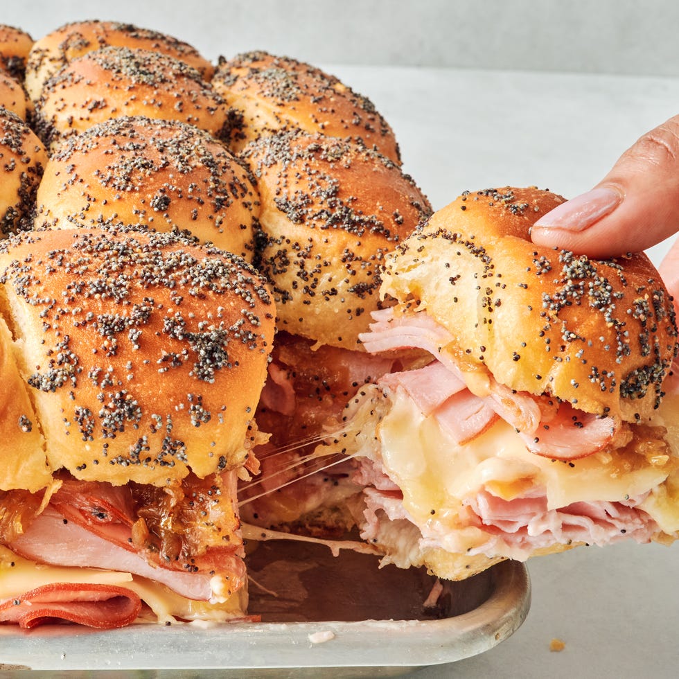 sliders stacked with sliced ham, swiss cheese, honey mustard, caramelized onions all between hawaiian rolls topped with a poppy seed dressing