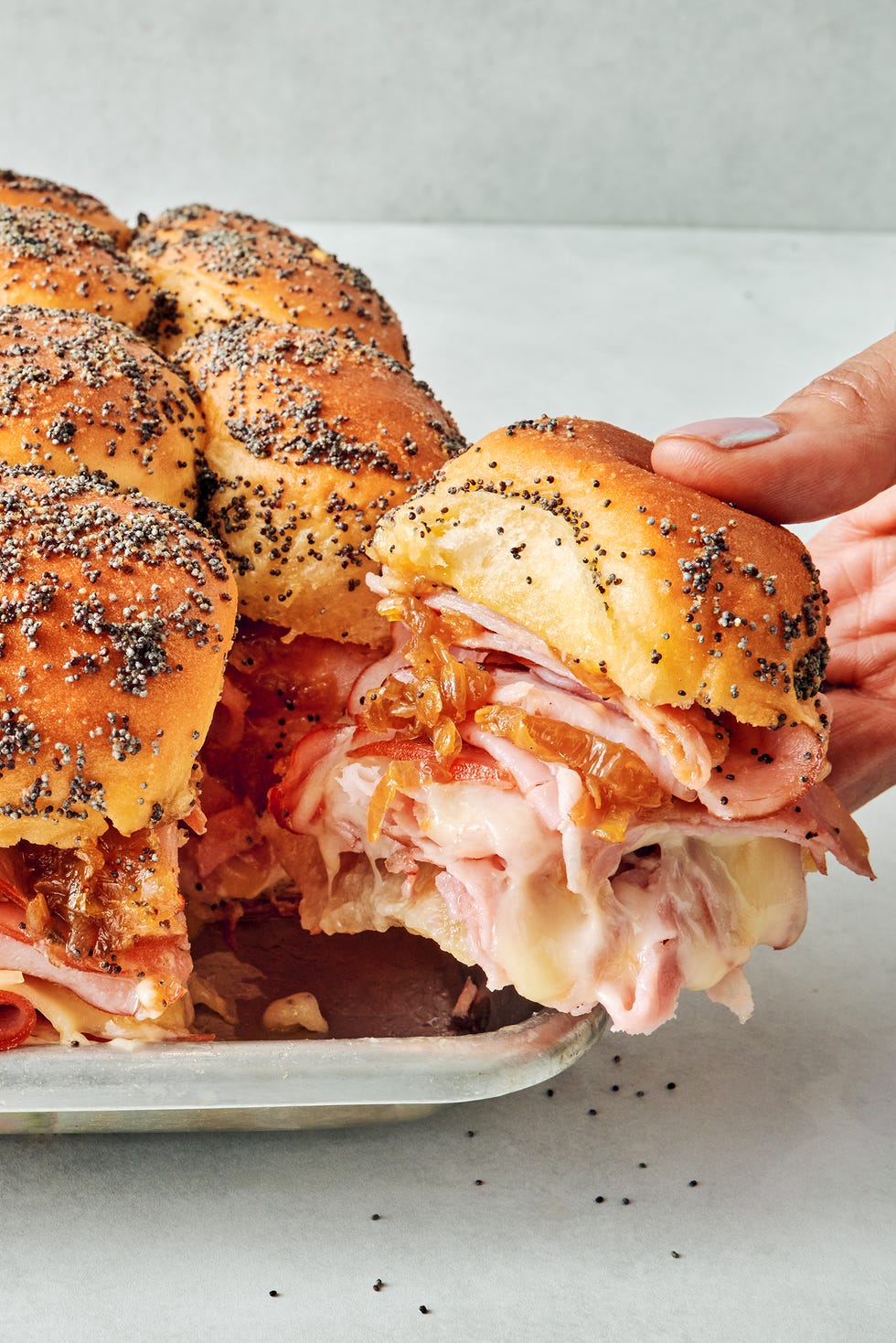 Hawaiian Roll Sliders sliders stacked with sliced ham, swiss cheese, honey mustard, caramelized onions all between hawaiian rolls topped with a poppy seed dressing