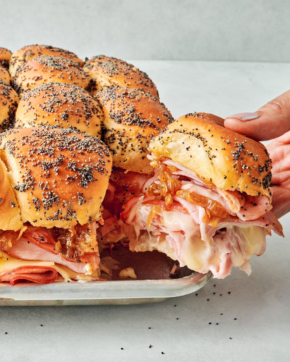 sliders stacked with sliced ham, swiss cheese, honey mustard, caramelized onions all between hawaiian rolls topped with a poppy seed dressing