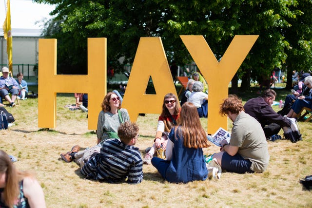 large yellow letters spelling hay with people sitting around on grass