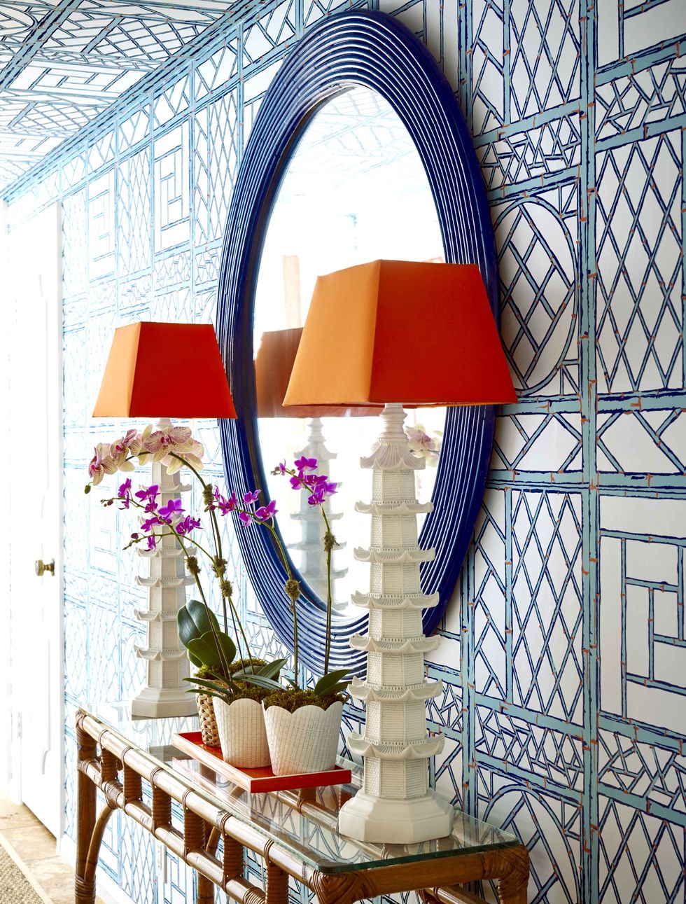 Wallpapered entryway with round blue mirror and two lamps