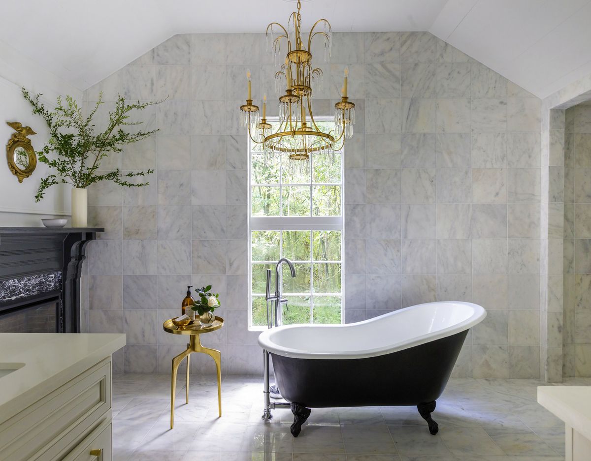 a classic black slipper tub anchors this spacious primary bathroom in the louisiana home of designer krystal matthews chandelier vintage tiles the home depot side table uttermost tub and fittings build with ferguson