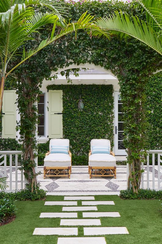 pavers set in grass lead through an ivy covered archway in this palm beach, florida, home by kemble interiors and smi landscape architecture chaise seating by celerie kemble on a mosaic tile patio invites relaxation