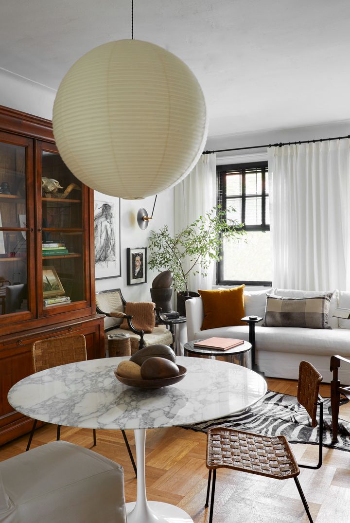 nyc apartment designed by david frazier living room with two distinct zones lounging and eating paint simply white, benjamin moore dining table eero saarinen, knoll chairs lee industries slipper vintage french rattan vintage kaare klint safari pendant isamu noguchi bookcase scott antique markets head vintage, high point market