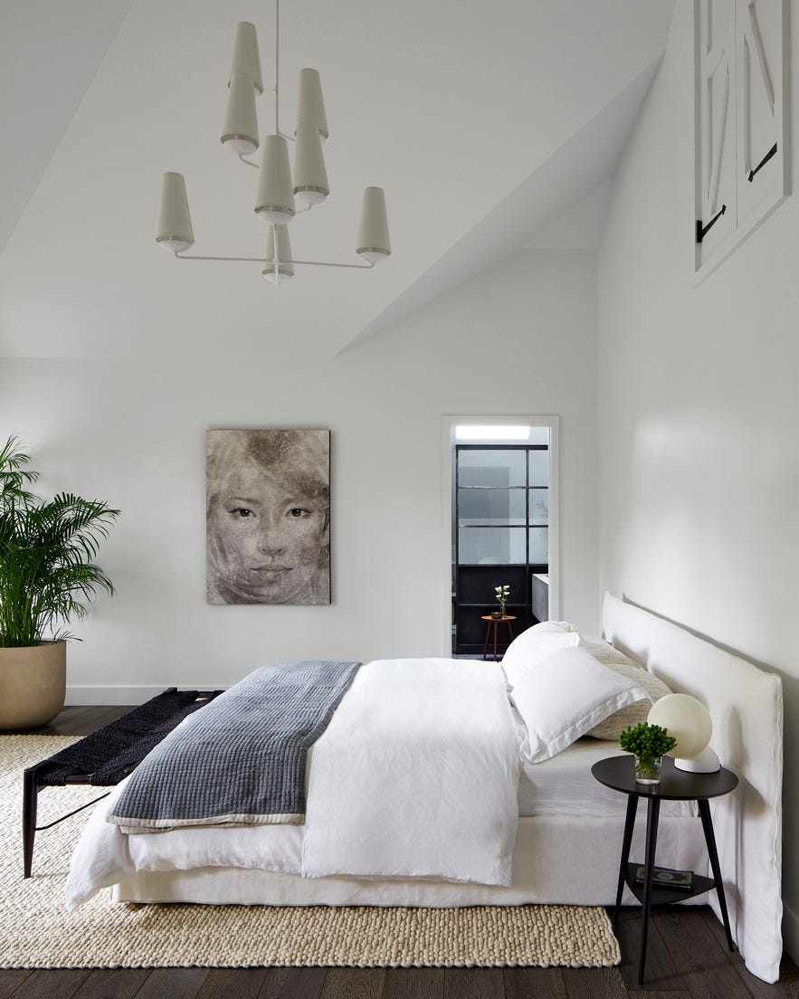 primary bedroom with soaring ceilings. chandelier: circa lighting. bed: gervasoni. bench: cb2. side table: room  board. rug: west elm. art: clients’ own. 19th century carriage house in montclair nj. interior design: elaine santos. design/architect: windigo architecture. minimal and modern accents. 