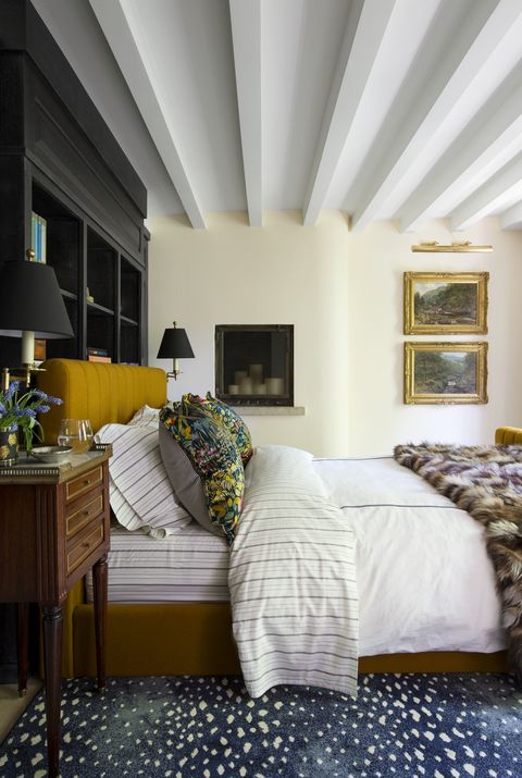 victorian turned postmodern townhouse in chicago by summer thornton design primary bedroom french attic aesthetic with beams, built in bookshelves behind the bed, and a mustard wool headboard wall paint adobe white, benjamin moore art alfred william rich bed custom, eli wyn upholstery, in fishman’s fabrics shams scalamandré sheets ralph lauren home