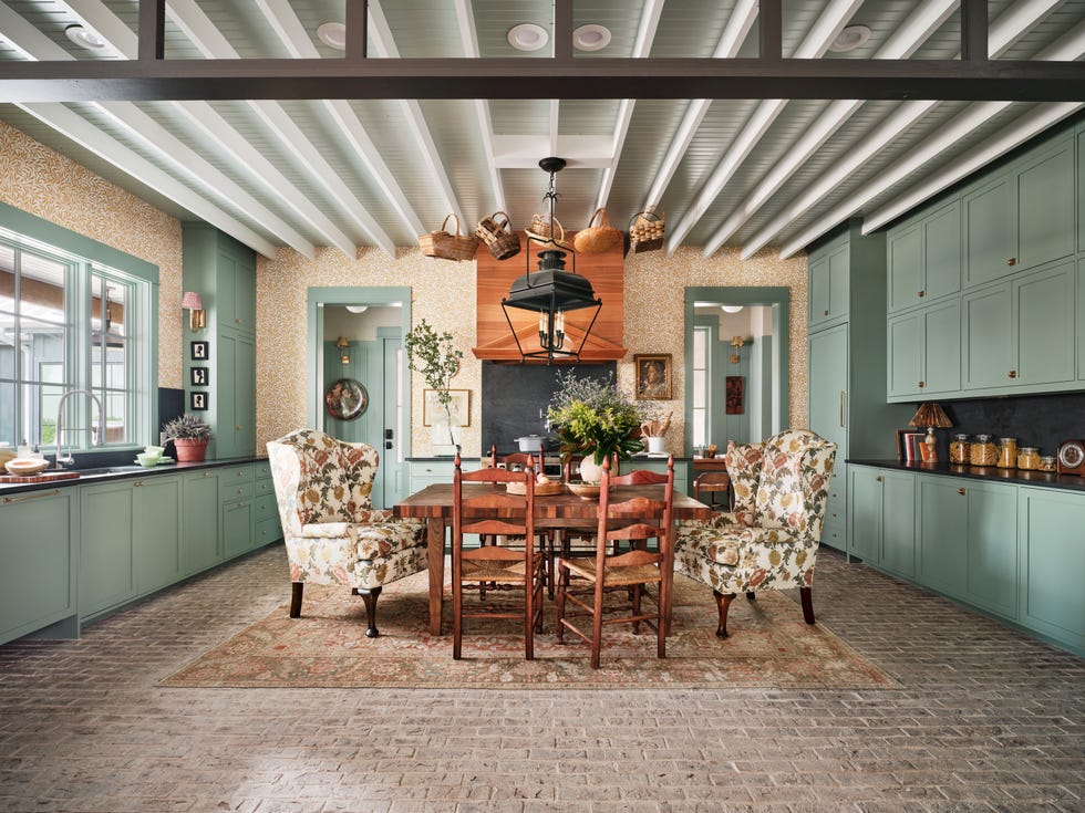 the gathering room. dining room table that seats six in the kitchen decorated with leaf motif wallpaper\, traditional wingback chairs (bought upholstered from an online consignor)\, blue green paint on the cabinetry and ceilings\, and a dark quartz countertop and backsplash. appliances: signature kitchen suite. fixtures: elkay. countertop and backsplash: caesarstone. table and range hood: grothouse. paint: farrow  ball. wallpaper: morris  co. lighting: circa lighting. rug: turkish carpets inc. door handle: schlage.