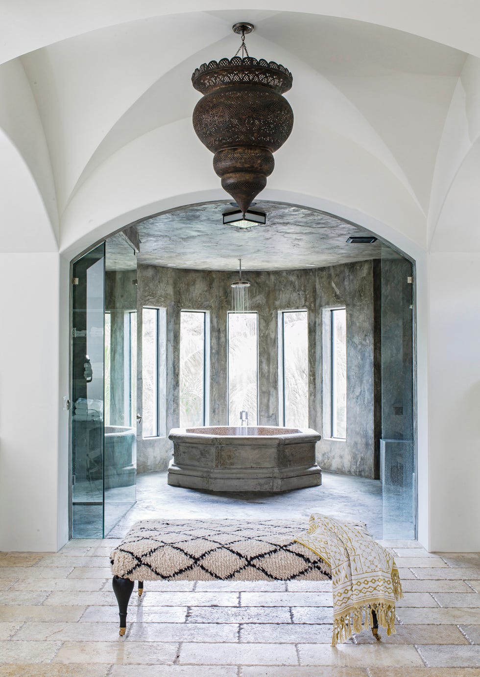 en suite bathroom the bathtub by ancient surfaces is a replica of an antique italian stone fountain. walls: custom concrete. chandelier: vintage moroccan. bench: custom. floor: reclaimed limestone.