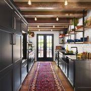 galley kitchen with white walls, black cabinets, wood floors and red runner rug facing french doors to the outside