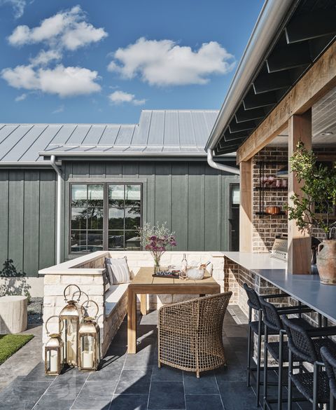 outdoor dining room with built in banquette, just opposite the cooking area dining table arhaus counter stools, dining chair, and metal lanterns frontgate