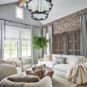 owners den, brick wall, white lounge sofa, white lounge chairs, throw rug, white and cream decorative cushions, gray walls, gray curtains, black candle ceiling light