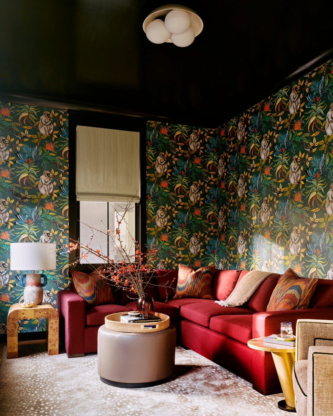den the bold colors and warm\, cocoon like vibe sofa custom\, in villa nova fabric wallpaper cole  son ottoman lee industries\, in pindler fabric red sofa\, tropical floral wallpaper with monkey print\, dark green\, dark ceiling\, roman shade\, dark decor\, rich colors living room a change of direction roaring gap, north carolina vacation home designed by liz carroll interiors architect clark tate colorful design 