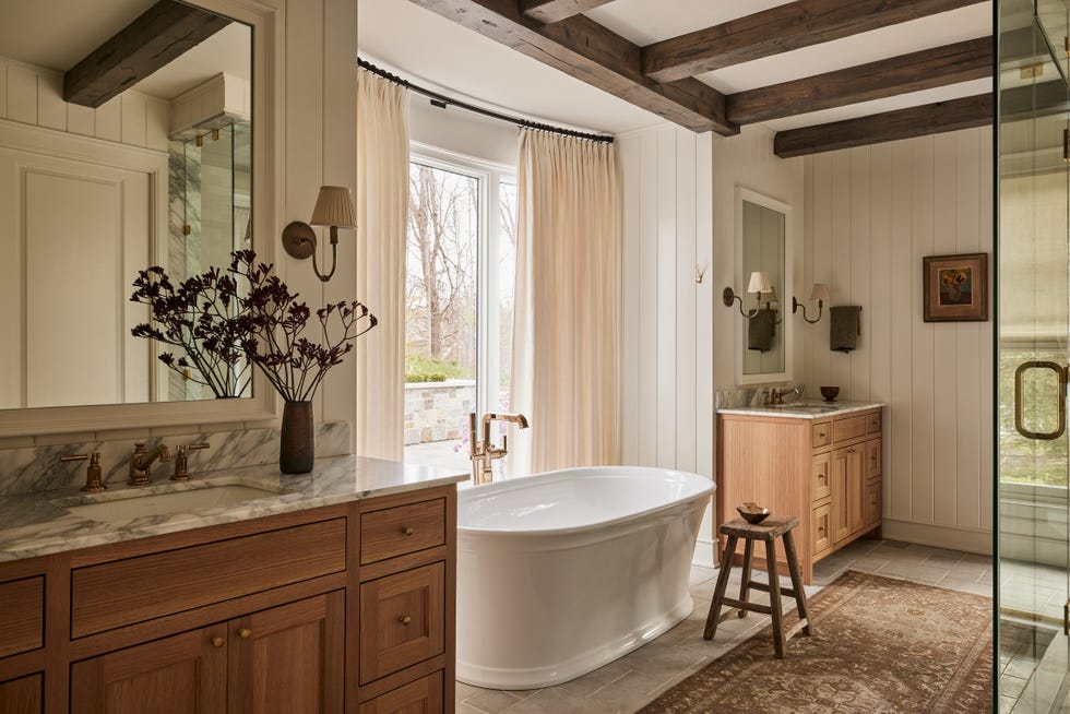 primary bathroom honed limestone flooring from zia tile is practical but not clinical. bathtub: kohler. fixtures: brizo. sconces: the urban electric co. quiet time: warm tones and natural textures took this indiana home from cavernous to cozy. warm neutrals, williams creek, indiana, georgian style residence, natural materials, wood accents.