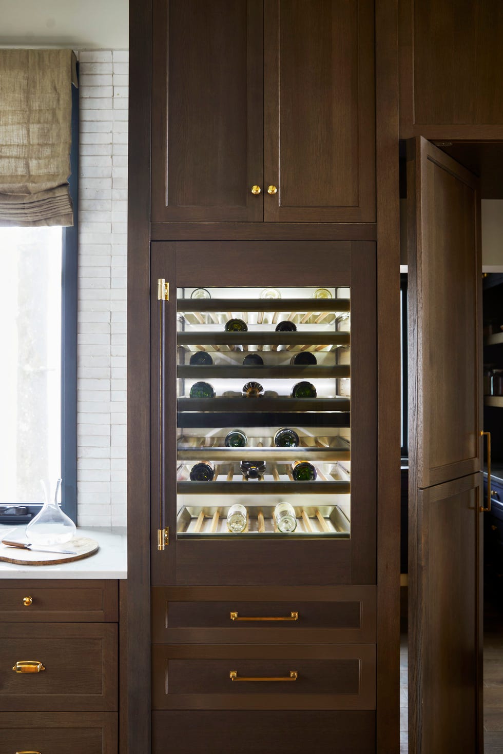 the kitchen. designed by kelsey leigh design co. @kelseyleighdesignco/kelsey mcgregor. natural finishes\, organic textures\, zellige tile\, a plastered range hood\, and complementary woods (white oak and maple) on the island and cabinetry. open glass shelves house pretty everyday tableware\, while closed drawer storage keeps pots and pans out of sight but accessible. includes "dirty kitchen"\, a hidden room accessed through french doors fabricated to look like cabinetry. appliances: monogram. roman shades: hunter douglas. fixtures: kohler. wine storage\, monogram 30" fully integrated wine sommelier refrigerator\, cabinet pulls and knobs: wayfair professional. whole home 2024. this year’s energy efficient home is in the conservation minded community of sprout\, located on a private nature preserve in hendersonville\, north carolina.