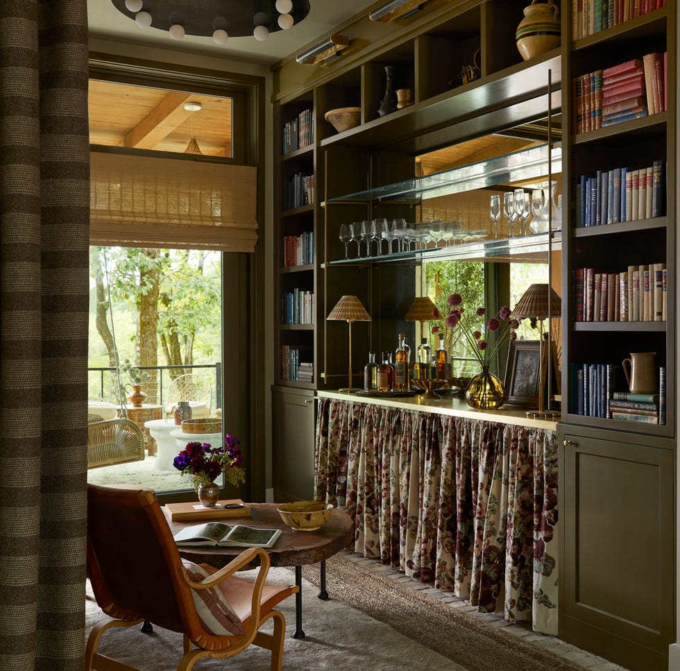 reading room: anne mcdonald design @anne_mcdonald_design. intimate, cozy retreat, custom millwork, luxurious solitude, antiqued mirror and brass shelf brackets from architectural grille, floating shelves, the bottom half of the built in is dressed with a floral skirt, softening the boxy architecture of the petite space. tactile elements, like a midcentury chair, 1970s limestone console, and silky goat hair rug, encourage guests to cross the threshold. to top it all off, a visual comfort  co. chandelier with alabaster globes adds a touch of vintage glamour overhead. balancing the hard and soft here was all about a curated mix of textures. shelf hardware brackets and cafe curtain rod: architectural grille. lighting: visual comfort  co. shades: hunter douglas. drapery: clarence house. rugs: safar (top), fibreworks (bottom). whole home 2024. this year’s energy efficient home is in the conservation minded community of sprout, located on a private nature preserve in hendersonville, north carolina.