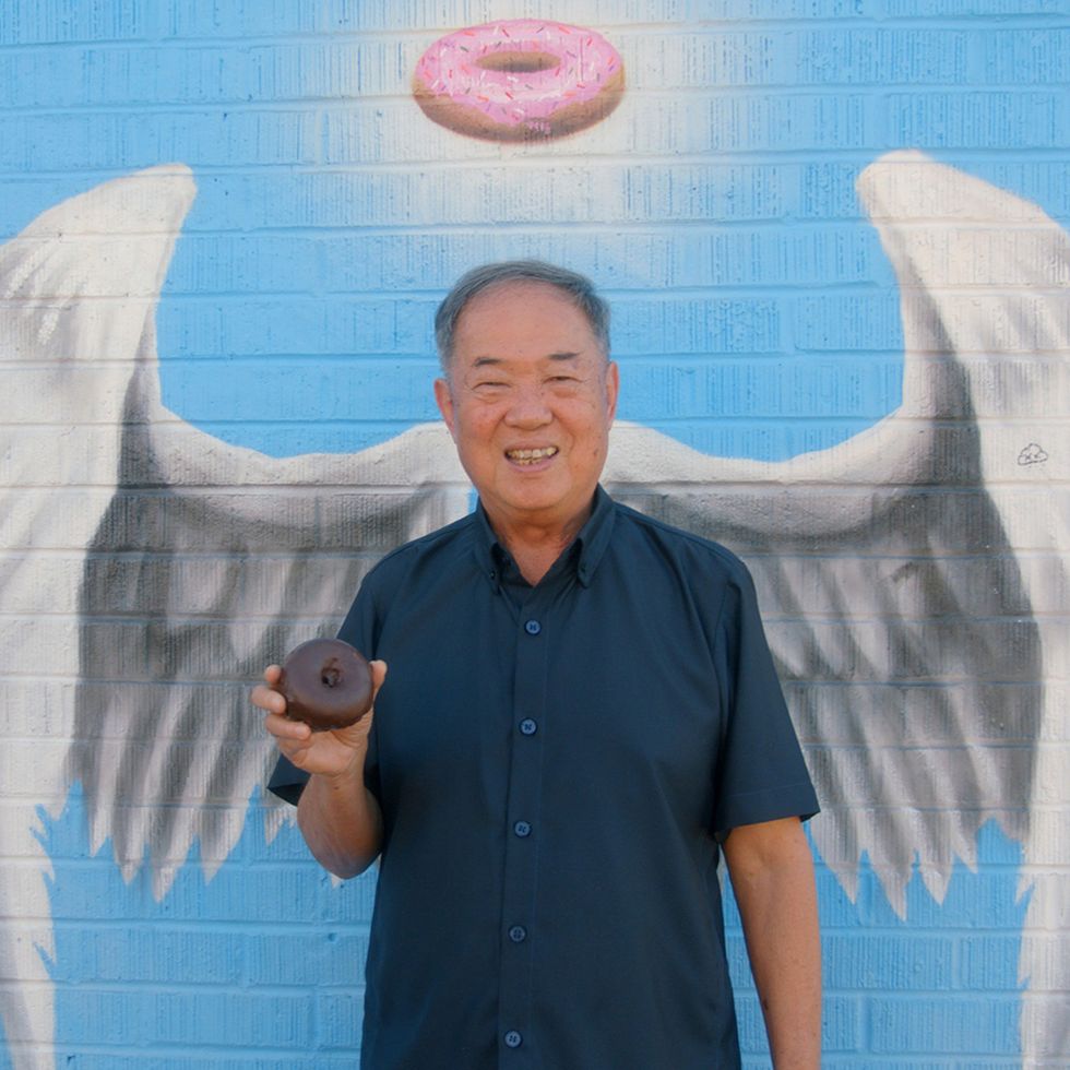 the donut king, donut king ted ngoy poses in front of the angel wings mural at dk's donuts, santa monica, california, 2020 © greenwich entertainment  courtesy everett collection