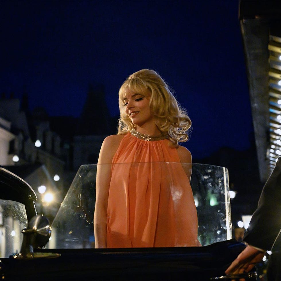 woman in a flowing coral dress standing near a classic car at night