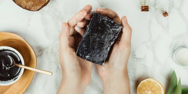Flatlay of woman's hands holding homemade charcoal soap with its ingredients on the side