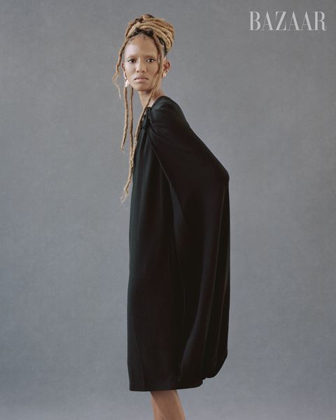 model stands with body in side profile and face facing the camera wearing a big black cape dress