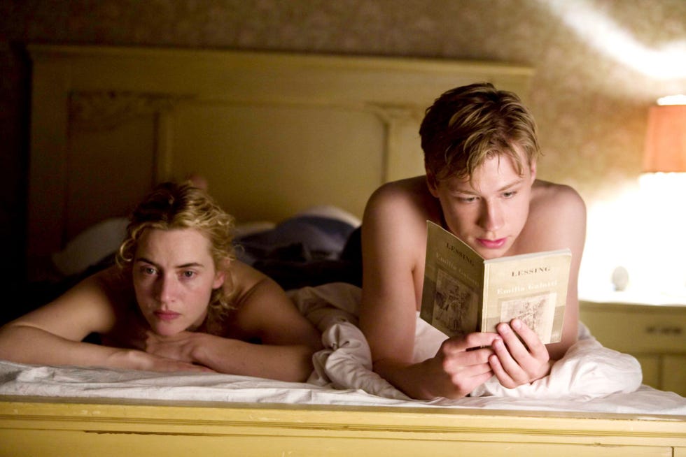 two individuals in bed one reading a book