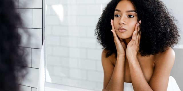 mixed race woman massaging her face and looking at a mirror
