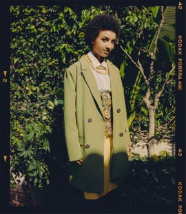 model wearing a green oversized coat and a yellow skirt in a lush outdoor setting