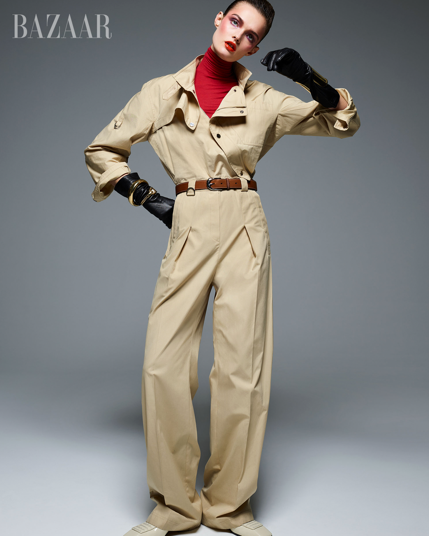 fashion model wearing a stylish beige jumpsuit with a red turtleneck and statement gloves